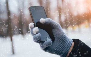 Handy-Reparatur: Eine Hand mit Handschuh hält ein Smartphone, während es im Hintergrund schneit