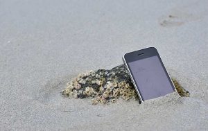 Handy-Reparatur: Ein Smartphone verschwindet halb in feuchtem Sand